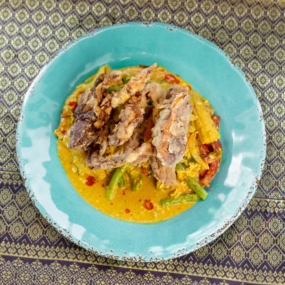 Fried soft-shell crab with yellow curry, vegetables, and red peppers on a blue plate.