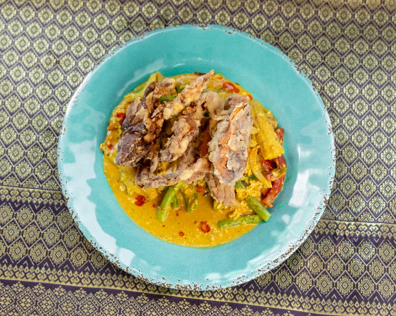 Fried soft-shell crab with yellow curry, vegetables, and red peppers on a blue plate.