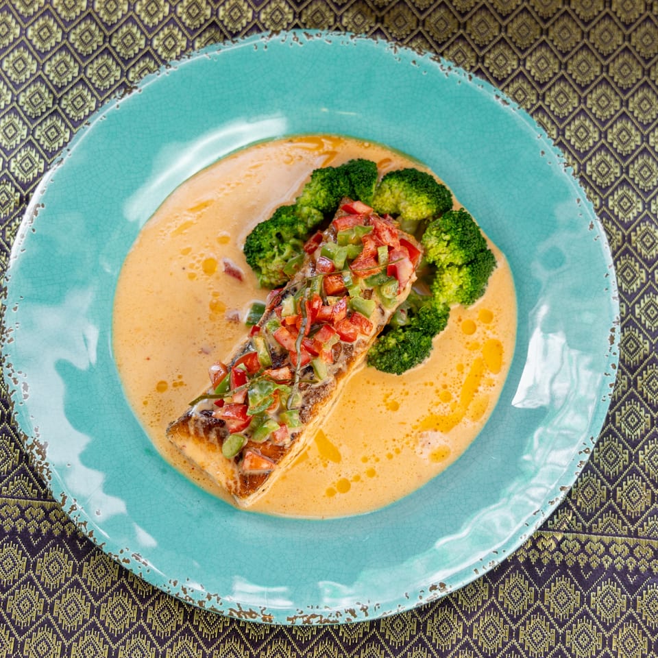 Salmon fillet with diced peppers and broccoli in a creamy sauce on a blue plate.