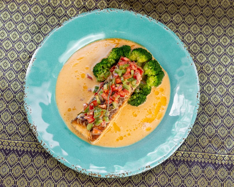 Salmon fillet with diced peppers and broccoli in a creamy sauce on a blue plate.