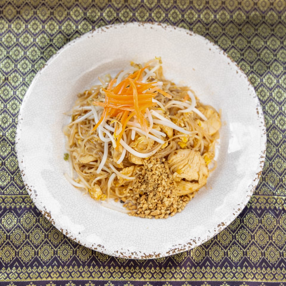 Chicken Pad Thai with bean sprouts, shredded carrots, and crushed peanuts on a white plate.