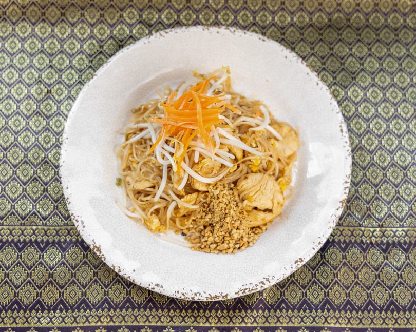 Chicken Pad Thai with bean sprouts, shredded carrots, and crushed peanuts on a white plate.
