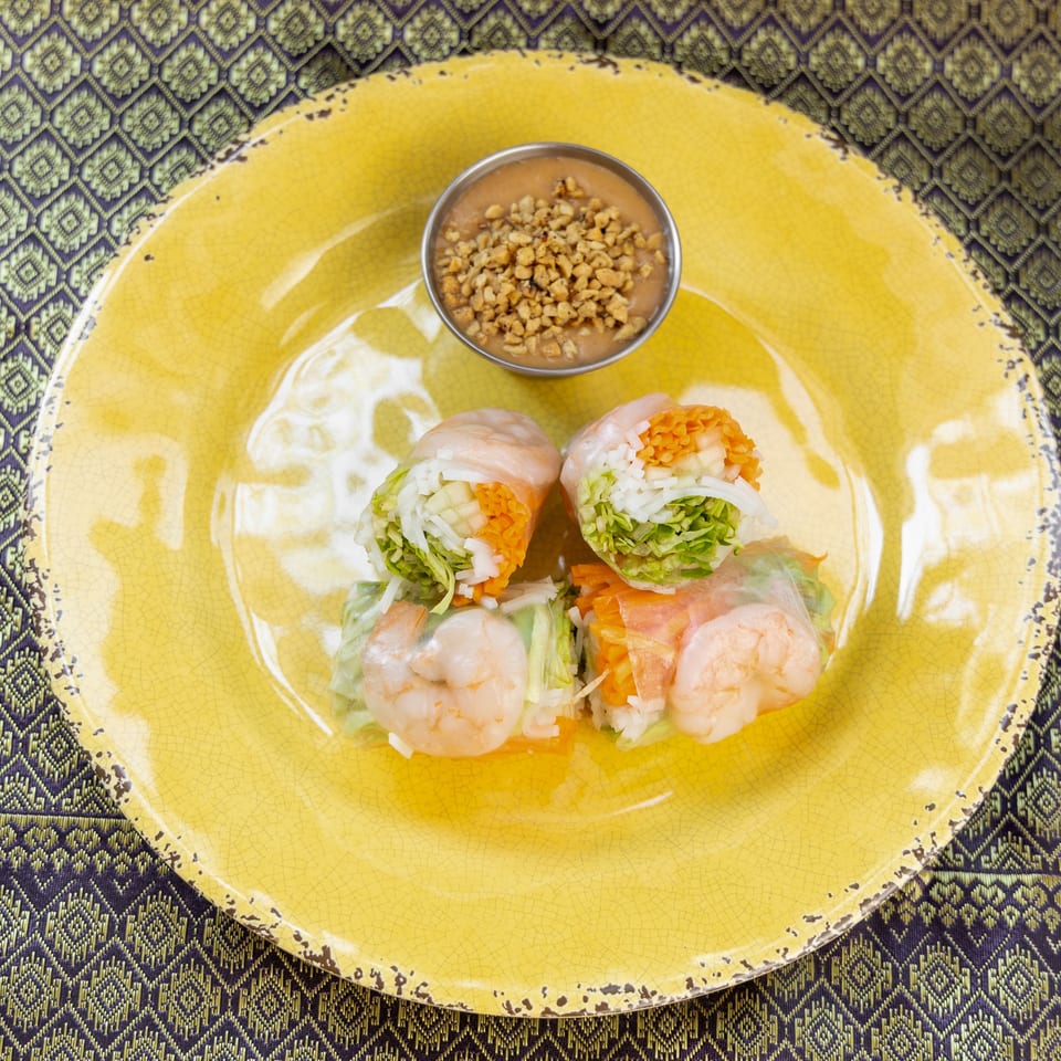 Four fresh spring rolls with shrimp, vegetables, and rice noodles, served with peanut sauce.