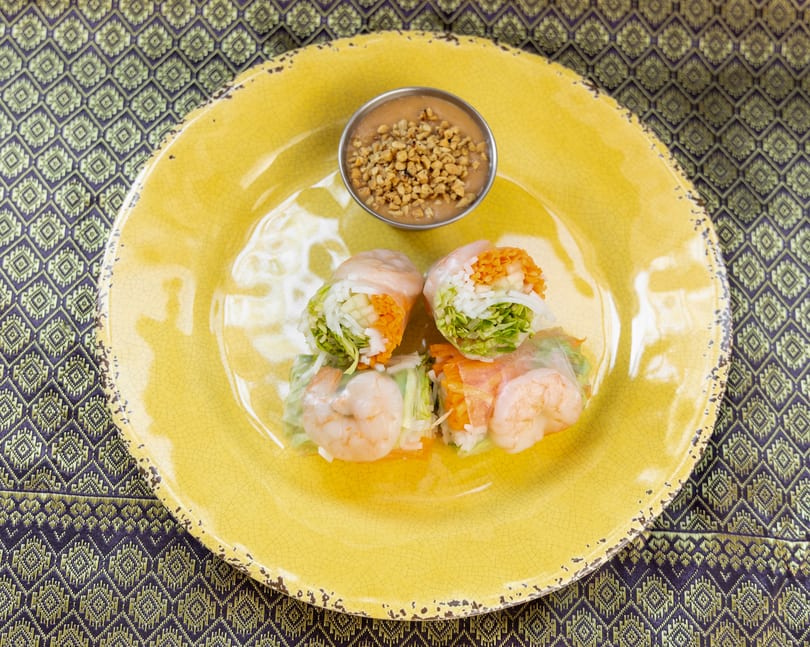 Four fresh spring rolls with shrimp, vegetables, and rice noodles, served with peanut sauce.